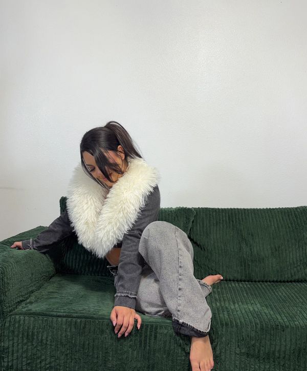 Woman sitting on a green couch wearing a jacket with a fluffy white collar.