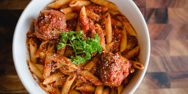 Bowl of penne pasta with meatballs and tomato sauce.