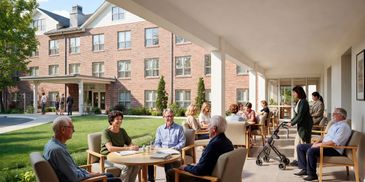 Seniors socializing outdoors on a covered patio with a brick building in the background.