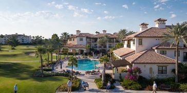 Luxury resort with pool and golf course under a blue sky.
