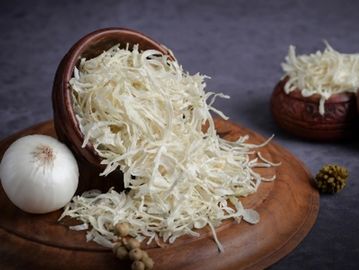 Grated white onion spilling from a wooden bowl onto a wooden plate.