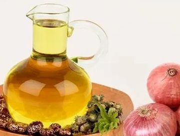 Glass jug of oil with onions and herbs on a wooden tray.