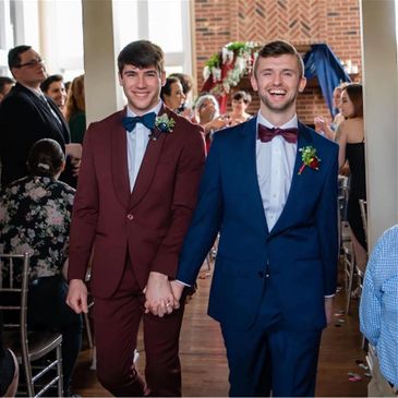Two men in suits holding hands and smiling at a formal event.
