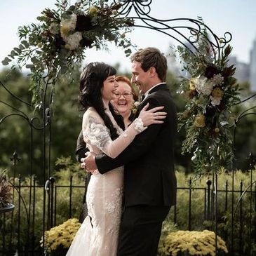 Bride and groom embracing under floral arch during outdoor wedding ceremony.