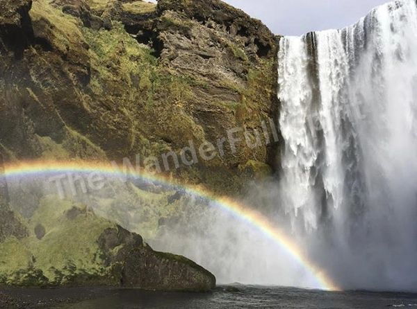 Waterfall in Iceland cascading with a vibrant rainbow arching at its base.