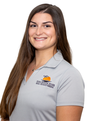 Smiling woman in a grey polo shirt with a real estate logo.