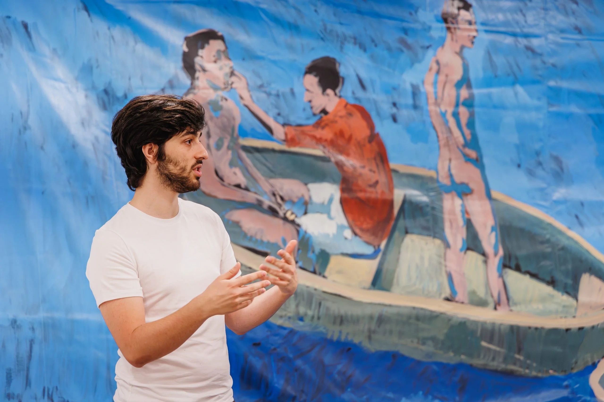 Photo of Diogo Nogueira in front of one of his paintings of men in a rowboat