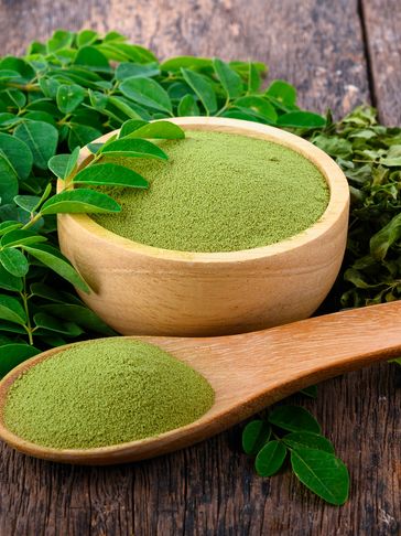 Organic Moringa oleifera powder displayed with fresh and dried Moringa leaves on a wooden table