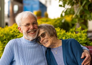 Two Senior Citizens sitting on a bench hugging and smiling.