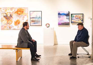 A father and son sit looking at each other in a photo gallery