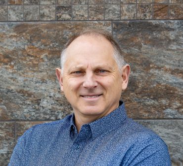 A man wearing a blue shirt looks into the camera. 