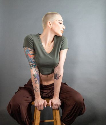 A woman with a shaved head sits on a stool.