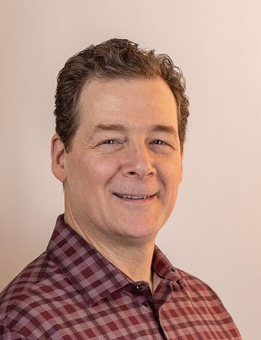 A man in a checkered shirt looks into the camera.