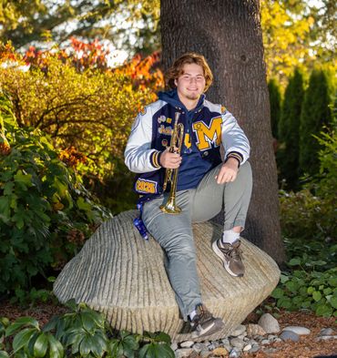 A High School Senior holding a trumpet and wearing a letterman jacket sitting for his Senior Photo.