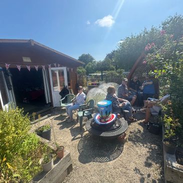 People enjoying a sunny outdoor gathering in a garden with chairs and decorations.
