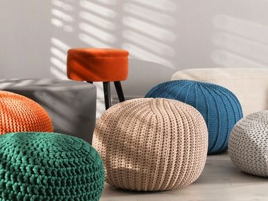 Colorful knitted poufs and an orange stool in a sunlit room.