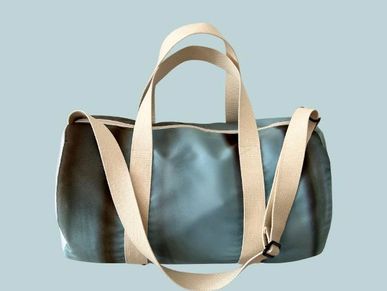 Minimalist gray duffel bag with beige straps on a soft blue background.