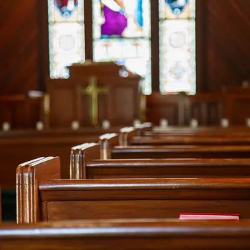 Empty wooden pews inside a church with stained glass windows.