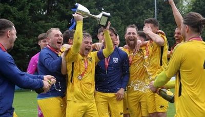 Soccer team celebrating with trophy and champagne on field.