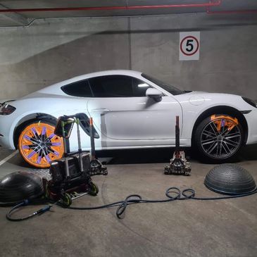White sports car in a garage with rear wheels being worked on.