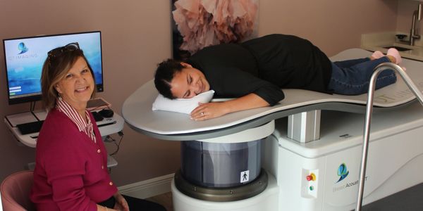 A woman lying on a medical scanning machine while another woman smiles nearby.