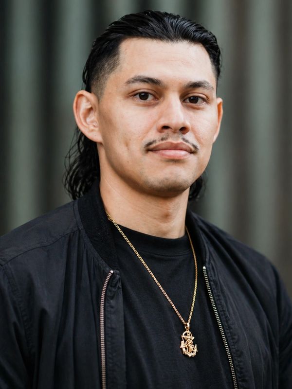 Man with slicked-back hair, black jacket, and gold anchor necklace.