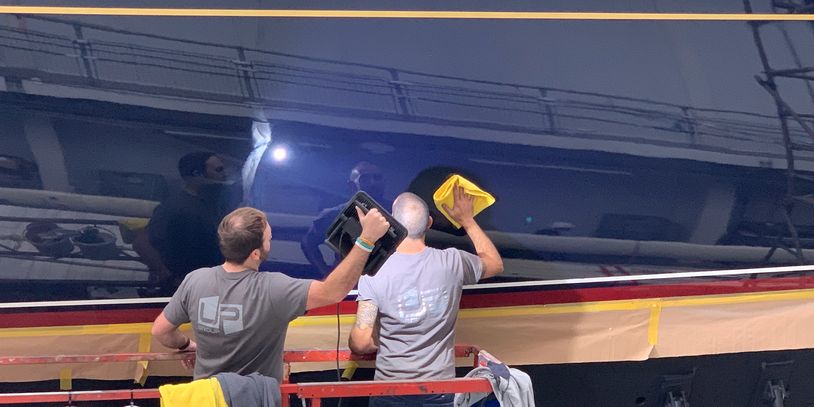 UP Group team members applying final stages to yacht exterior finishing in high gloss blue.