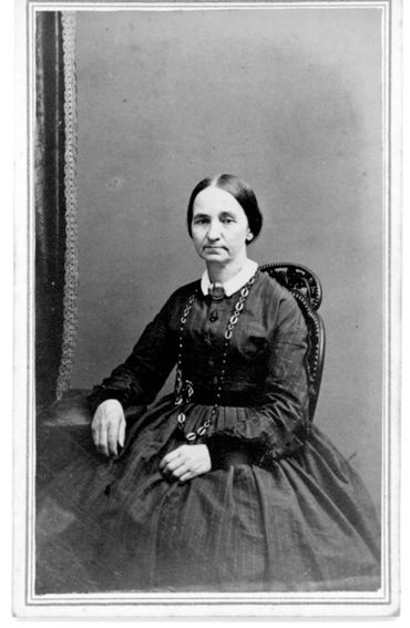 Photo of a woman seated at a table. The woman has her hair pulled back and is wearing a long necklac