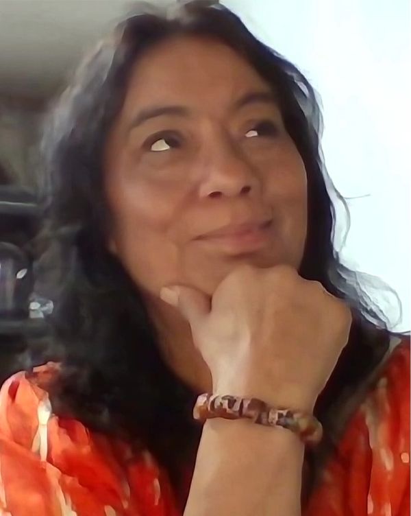 Woman in orange shirt looking thoughtfully upward with hand on chin.