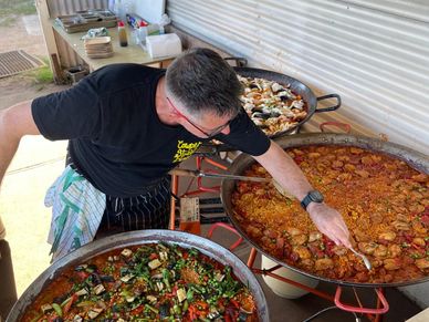 Chef preparing large pans of colorful paella outdoors.