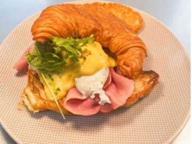Croissant sandwich with ham, poached egg, greens, and hollandaise sauce.