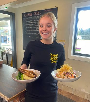 Smiling waitress holding two plates of food inside a diner.