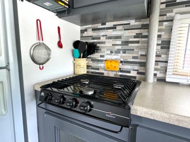 Modern kitchen stove with utensils hanging on the wall.