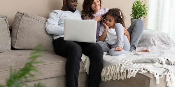Family of three using a laptop while sitting on a sofa.