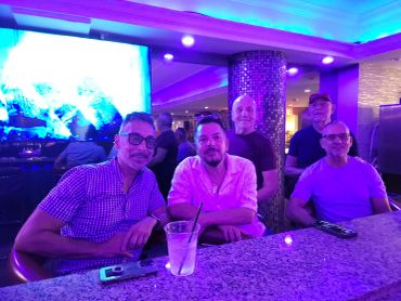 Five men sitting at a bar with blue lighting.