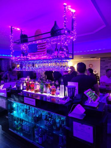 Vibrant bar illuminated with purple lights and decorated with string lights.