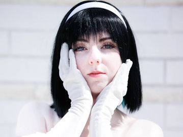 Portrait of a person with black hair and white gloves.