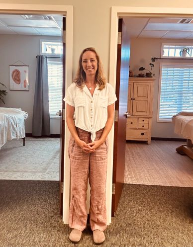 Woman standing in doorway between two rooms, smiling.