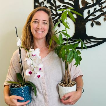 Woman smiling, holding two potted plants.