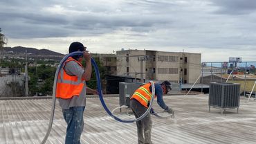Trabajadores aplicando recubrimiento en techo industrial.