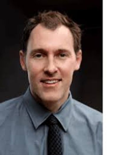 Professional portrait of a man in a blue shirt and dark tie.