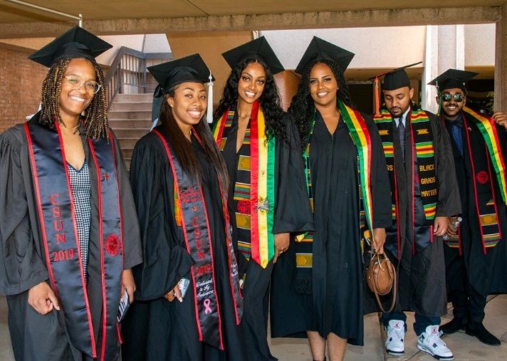 Group of diverse graduates in caps and gowns smiling together.