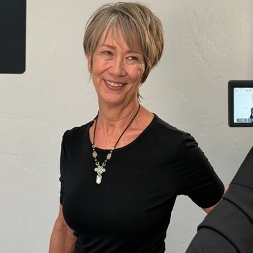 Smiling woman wearing a black top and necklace in a studio setting.
