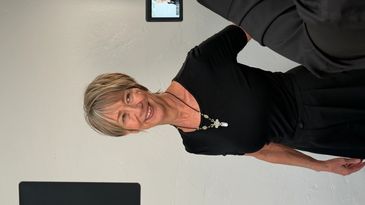 Smiling woman wearing a black top and necklace in a studio setting.