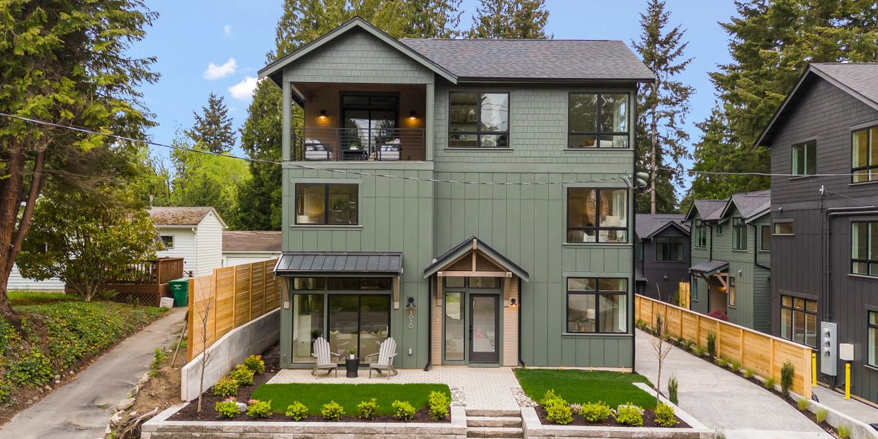 Modern green three-story house with balcony and landscaped front yard.