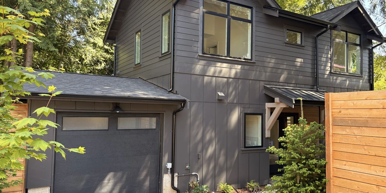 Modern dark gray two-story house with attached garage and wooden fence.