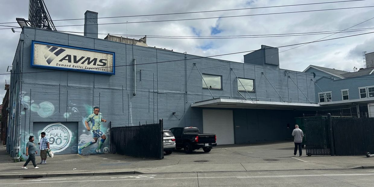 A gray building with a soccer mural and three people nearby on a cloudy day.