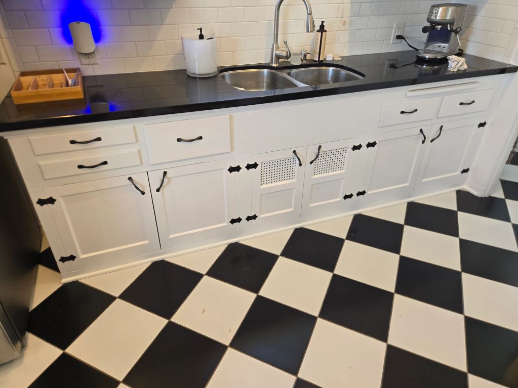 Clean kitchen sink with black countertop and checkered floor.