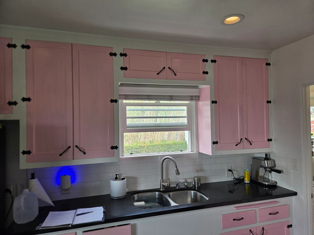 Kitchen with pink cabinets and black countertop under a window.