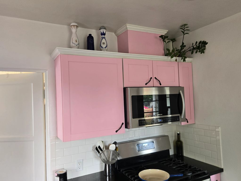 Pink kitchen cabinets with stove and decorative bottles.